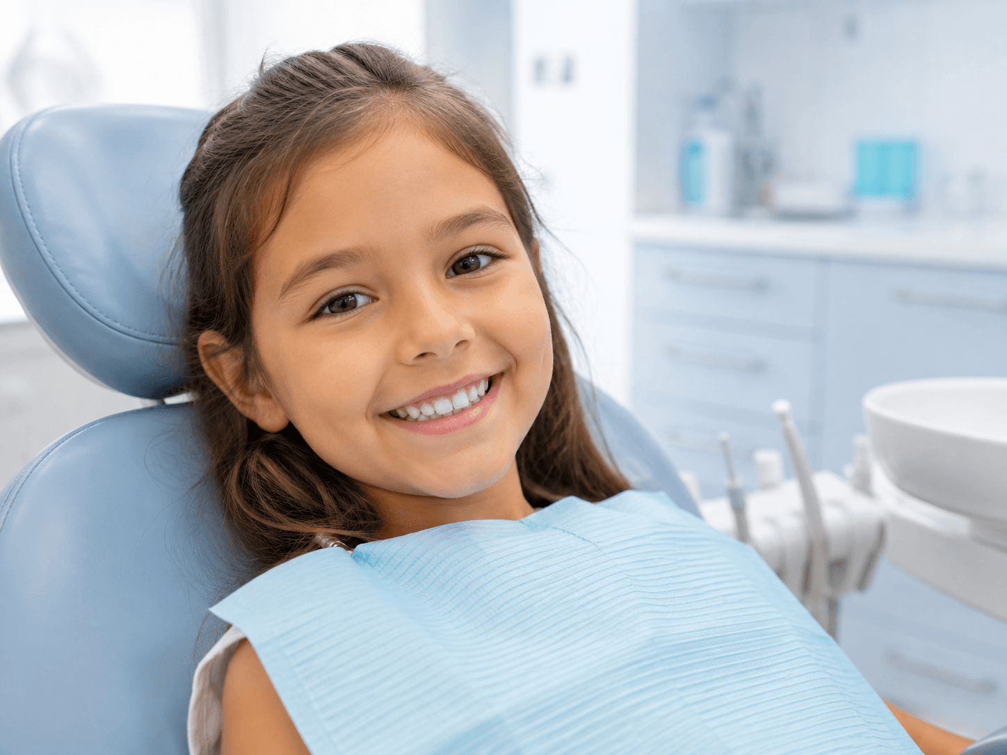 Niña sonriente en el sillón dental, con las muelas ya protegidas con sellantes